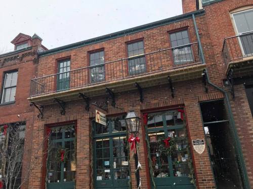 A brick building with large windows, festive decorations, and a snow-covered streetlamp in a quaint town setting.