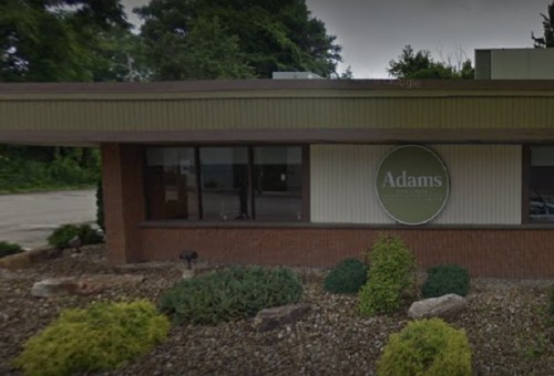 Exterior view of a building with a sign that reads "Adams" surrounded by greenery and landscaping.