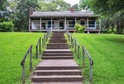 A historic house with a porch, surrounded by greenery, accessed by a set of stone steps.