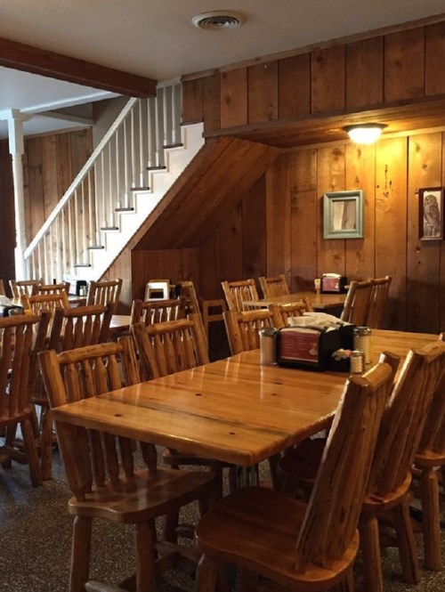 Cozy wooden dining area with rustic tables and chairs, featuring a staircase and wooden paneling on the walls.