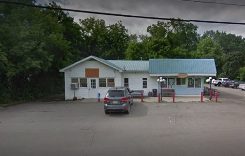 A small, single-story building with a green roof, surrounded by trees, and a parked car in front.