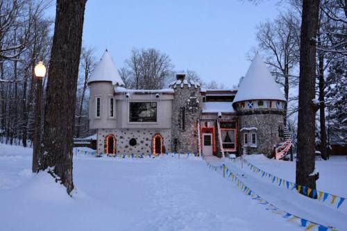 A whimsical stone castle with turrets, decorated for winter, surrounded by snow and trees.