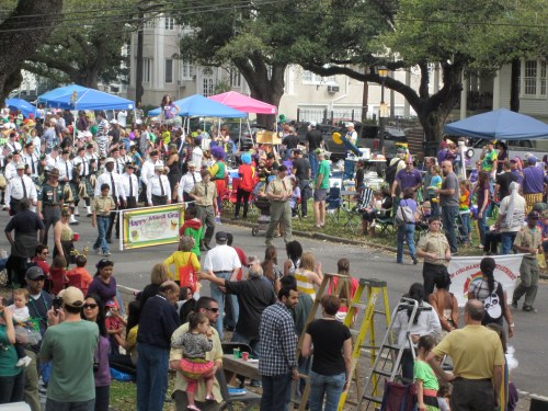 A lively outdoor festival with colorful tents, people in costumes, and a parade atmosphere filled with families and activities.