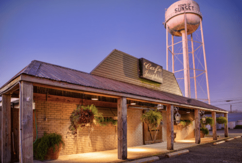 A rustic café with a sign reading "Cafe Josephine" and a water tower in the background, illuminated at dusk.