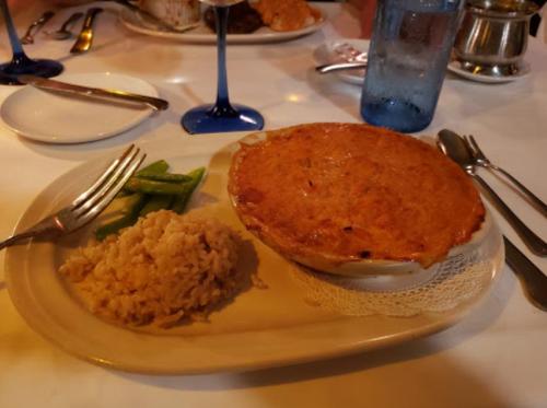 A plate with a baked dish, rice, and green beans on a table set with utensils and glasses.