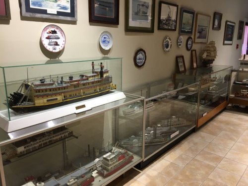 Display of model ships in glass cases, with framed maritime art and decorative plates on the walls.