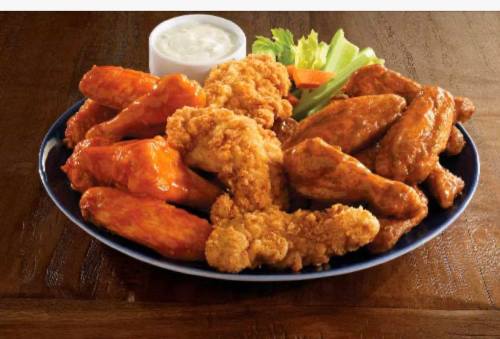 A platter of chicken wings in various flavors, with a side of ranch dressing and fresh lettuce and carrots.