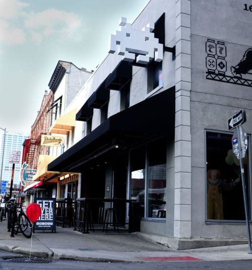 A street view of a building with a retro video game design, featuring a large pixelated character and a red balloon.