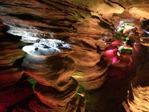 Colorful lights illuminate the textured rock formations inside a cave, creating a vibrant and mystical atmosphere.