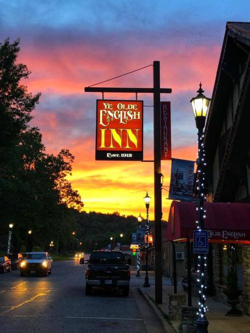 A sunset casts vibrant colors over a street with a sign for Ye Olde English Inn and lampposts lining the road.
