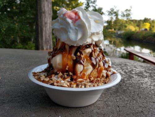 A delicious ice cream sundae topped with whipped cream, caramel, chocolate sauce, and nuts, served in a white bowl.