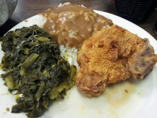 A plate of food featuring fried chicken, rice with brown gravy, and a side of collard greens.