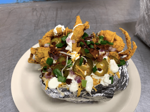 A loaded baked potato topped with fried okra, jalapeños, bacon, cheese, and drizzled with sour cream and green onions.