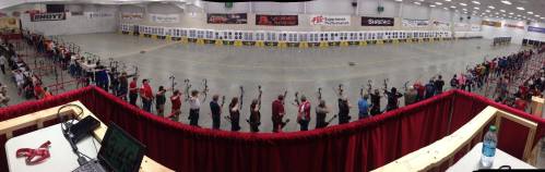 A panoramic view of an archery range with numerous archers lined up, preparing to shoot at targets in the distance.