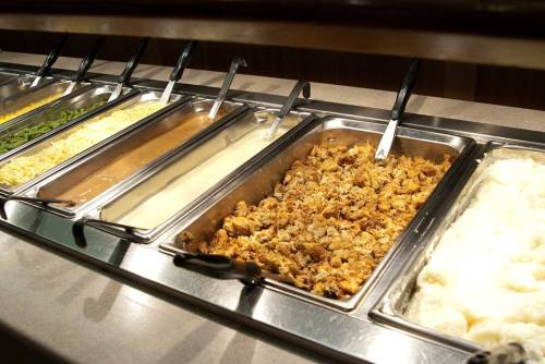 A buffet line featuring trays of green beans, cheese, gravy, stuffing, and mashed potatoes.