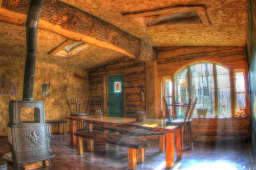 Cozy interior of a rustic room with wooden beams, a large table, and a stove, featuring stained glass windows.