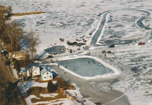 Aerial view of a frozen lake with people ice fishing and skating, surrounded by snow and ice-covered land.