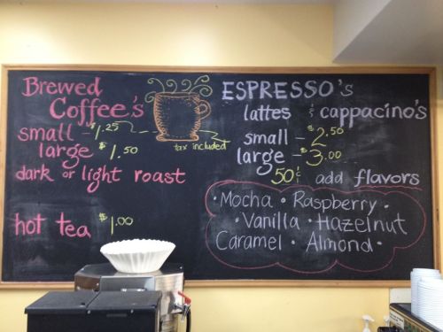Chalkboard menu listing brewed coffee, espresso drinks, and hot tea prices with flavor options.