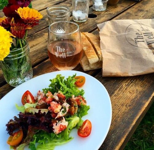 A fresh salad with lobster, cherry tomatoes, and greens, accompanied by a glass of rosé and a paper bag of bread.