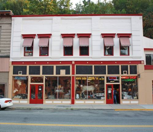 A vintage storefront with red accents, featuring an antique shop and a pawn shop, both with large display windows.