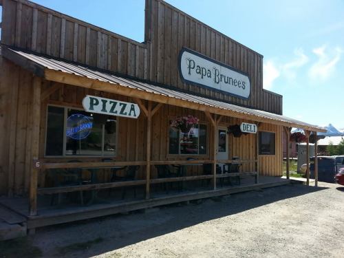 A rustic wooden building with a sign reading "Papa Brunee's," featuring "Pizza" and "Deli" signs and outdoor seating.