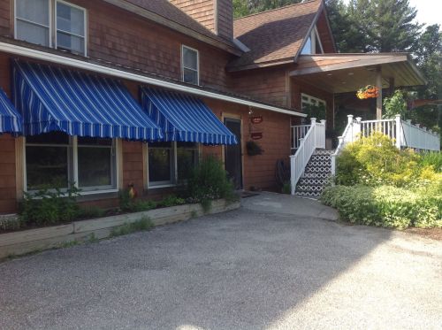 A charming brown house with blue striped awnings, a white staircase, and a landscaped garden in front.