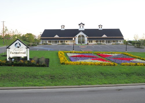 A large building with a black roof and white trim, surrounded by colorful flower beds and a sign for Berlin Farmstead.