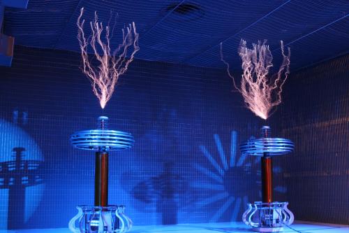 Two Tesla coils emitting electric arcs in a dark room with blue lighting, creating a dramatic visual effect.
