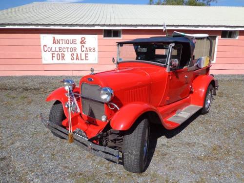 A bright red vintage car parked in front of a pink building with a sign that reads "Antique & Collector Cars For Sale."