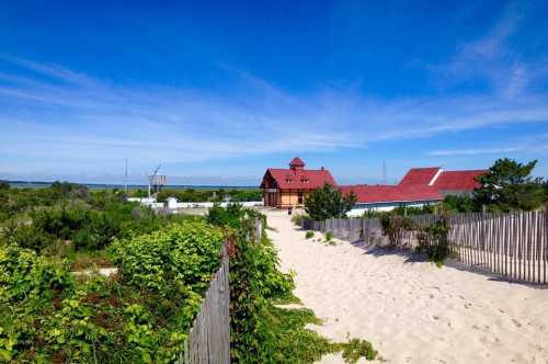 A sandy path leads to a red-roofed building surrounded by greenery under a clear blue sky.