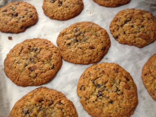 Freshly baked oatmeal chocolate chip cookies on parchment paper, golden brown and slightly chewy.