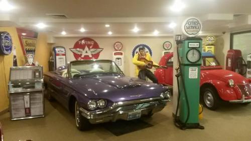 A vintage purple convertible car in a retro gas station display with old gas pumps and a musician statue.