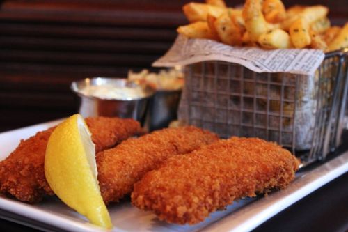 Crispy fried fish fillets with a lemon wedge, served alongside a basket of seasoned fries and a small cup of dipping sauce.