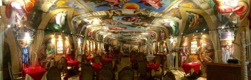 A lavish restaurant interior with ornate ceiling murals and elegantly set tables, creating a grand atmosphere.