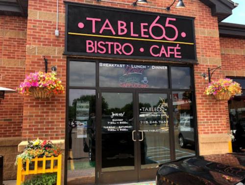 Exterior of Table 65 Bistro Café, featuring a colorful sign and flower baskets, with doors inviting customers inside.