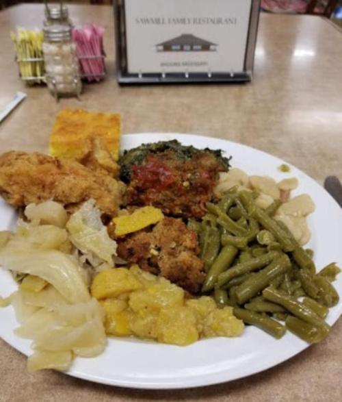 A plate of Southern comfort food featuring fried chicken, greens, cornbread, cabbage, green beans, and squash.