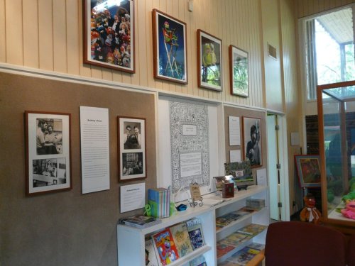 A wall display featuring framed photos and artwork related to puppetry, with shelves of books below.