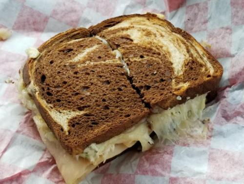 A sliced sandwich on marbled rye bread with sauerkraut peeking out, wrapped in red and white checkered paper.