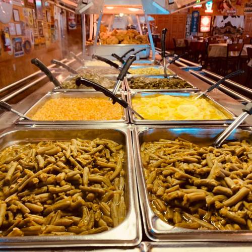 A buffet display featuring various dishes in metal trays, including greens, grains, and a yellow sauce.