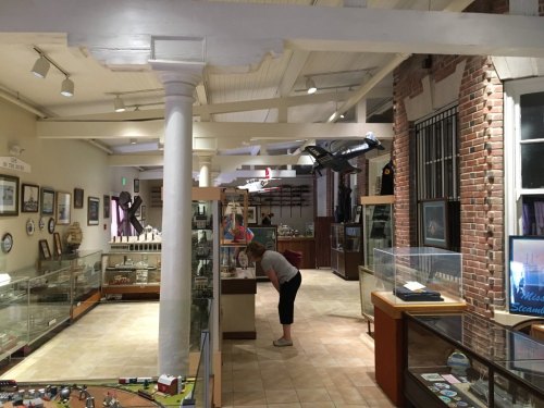 A museum interior featuring display cases, artifacts, and a visitor examining exhibits under bright lighting.