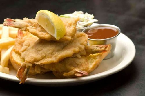 Fried soft-shell crabs with a lemon wedge, coleslaw, and dipping sauce, served with French fries on a plate.