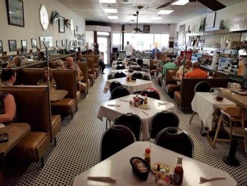 A bustling diner with booths and tables, patrons enjoying meals, and a counter with a cook in the background.