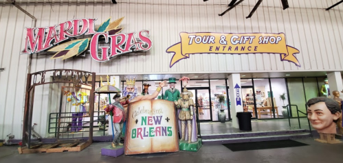 Entrance to a Mardi Gras tour and gift shop, featuring colorful signage and large decorative figures.