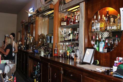 A rustic bar with shelves of various liquor bottles, wooden counters, and patrons in a lively atmosphere.