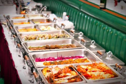 A buffet table with various dishes in metal trays, including seafood, meats, and colorful sides, set in a restaurant.
