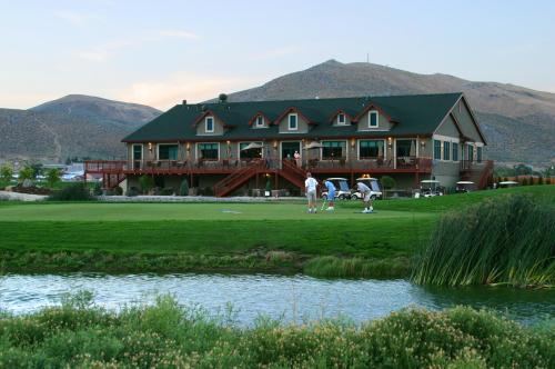A golf course clubhouse with a mountain backdrop, featuring golfers and golf carts near a pond.