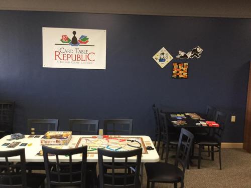 A board game lounge with a table set up for games, featuring various board games and a sign for "Card Table Republic."