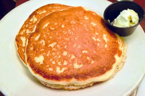 Three golden-brown pancakes served on a plate with a small cup of butter on the side.