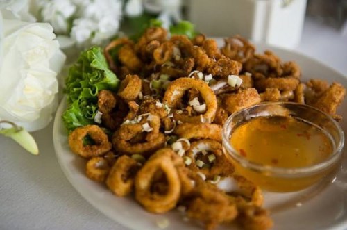 A plate of crispy fried calamari served with a side of dipping sauce and garnished with lettuce.