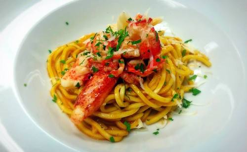 A plate of pasta topped with lobster meat and garnished with fresh herbs.